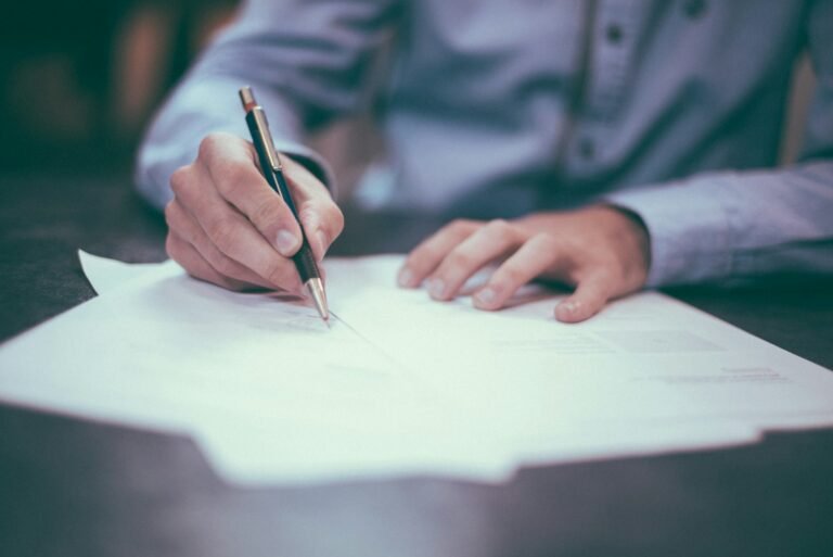 Mano firmando un documento con un bolígrafo sobre una mesa
